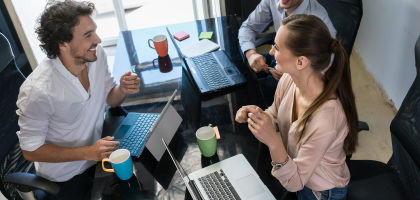 Młodzi ludzie siedzą przy laptopach postawionych na biurku.